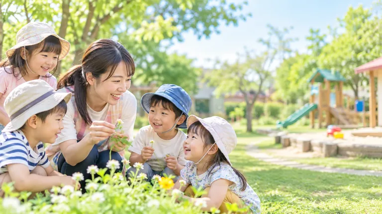園庭で草花を囲んで過ごす子どもたちと保育者
